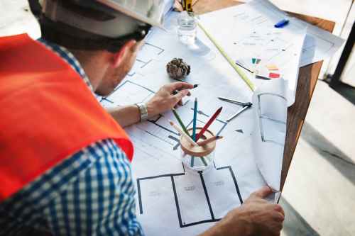 man wearing white hard hat leaning on table with sketch plans